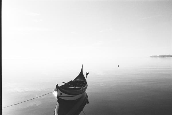 São Jacinto Nature Reserve, Aveiro, late 1990s. A small boat rests quietly on still water, tied yet appearing to float freely in the light. The horizon fades into the distance, merging sky and river into one. A moment of calm, where simplicity and silence speak louder than detail.